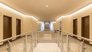 A modern hotel corridor with glass railings, wooden doors, and a central elevator. - ARIBO Hotel Erbendorf (Erbendorf)