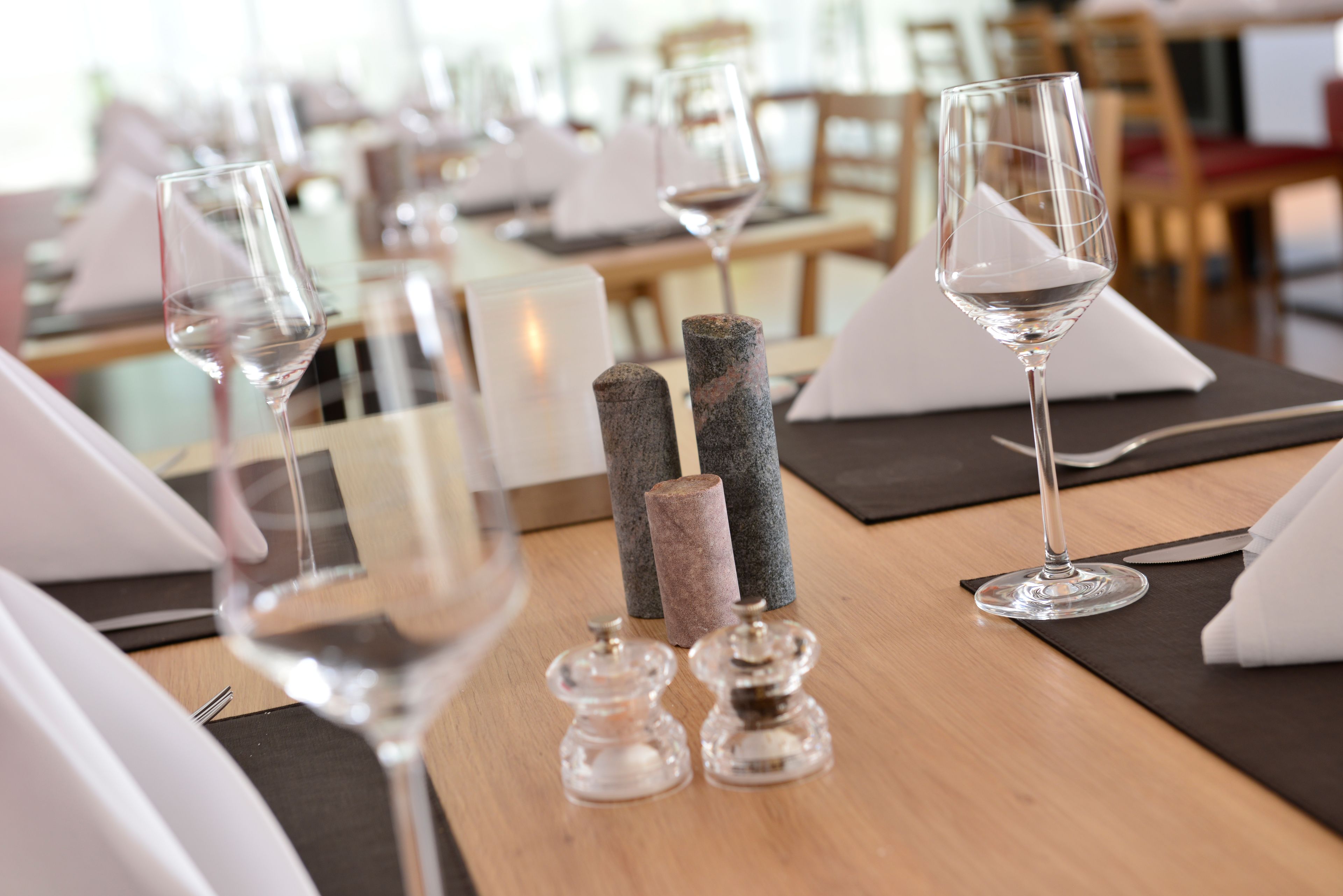 Une table à manger dressée avec des verres à vin, des salières et des poivrières, et une serviette.