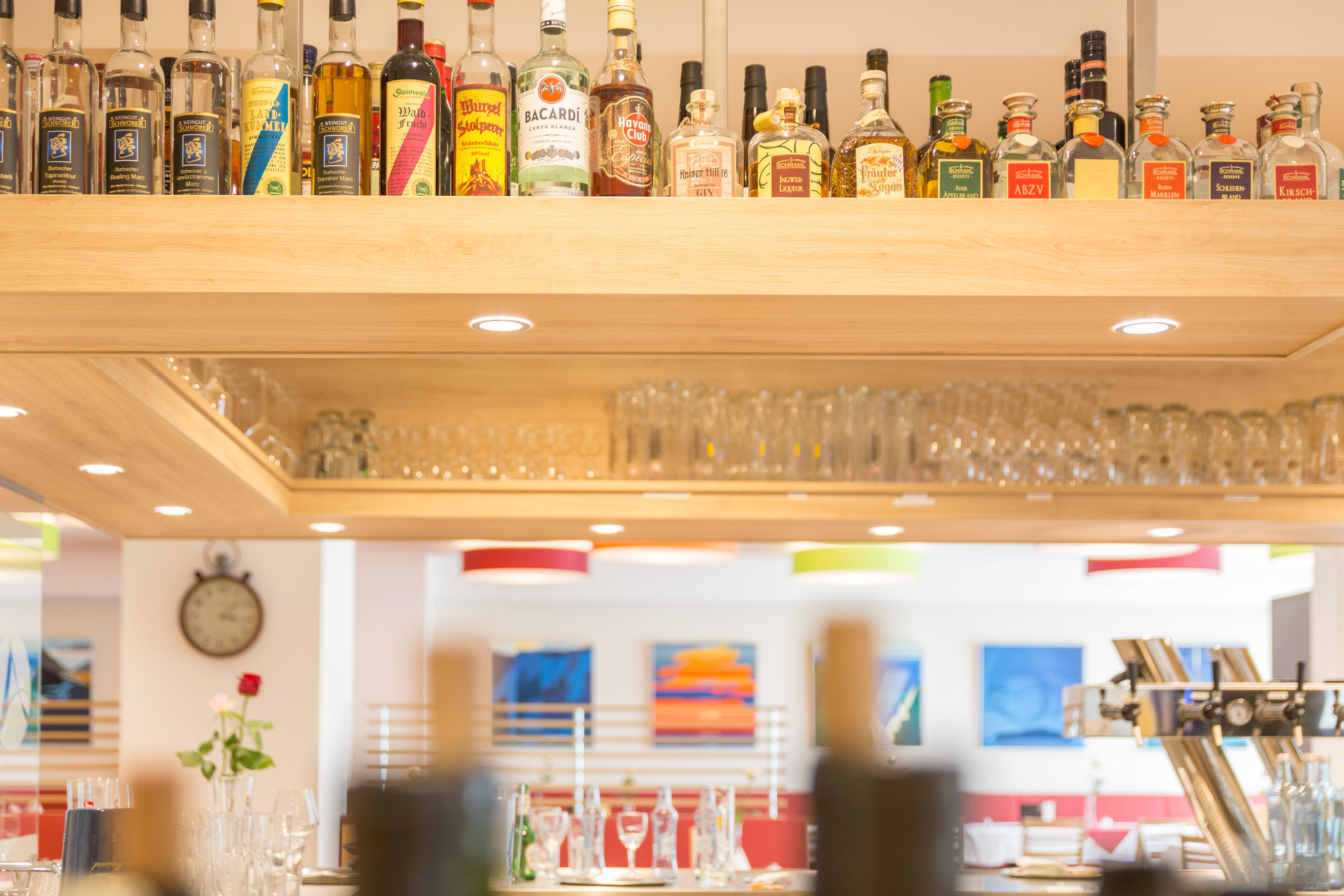 Zona de bar con varias botellas de licores y copas en estanterías.