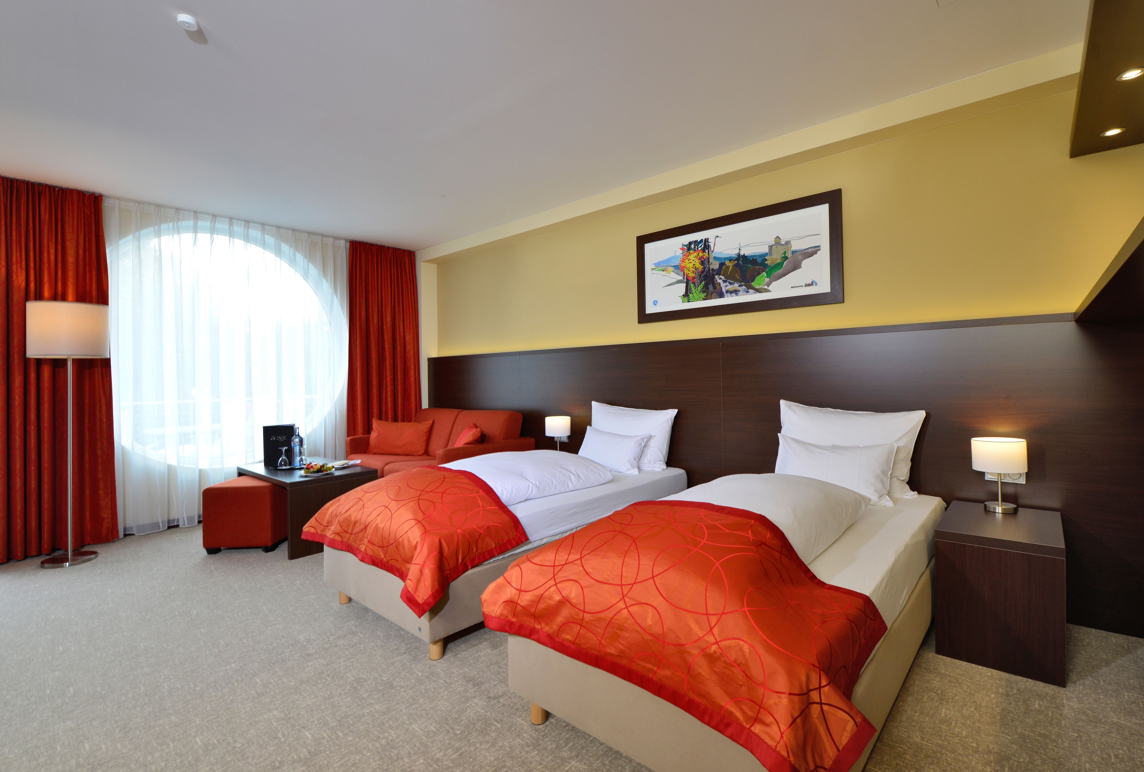 A hotel room with two beds, a desk, a chair, a lamp, and a painting on the wall.