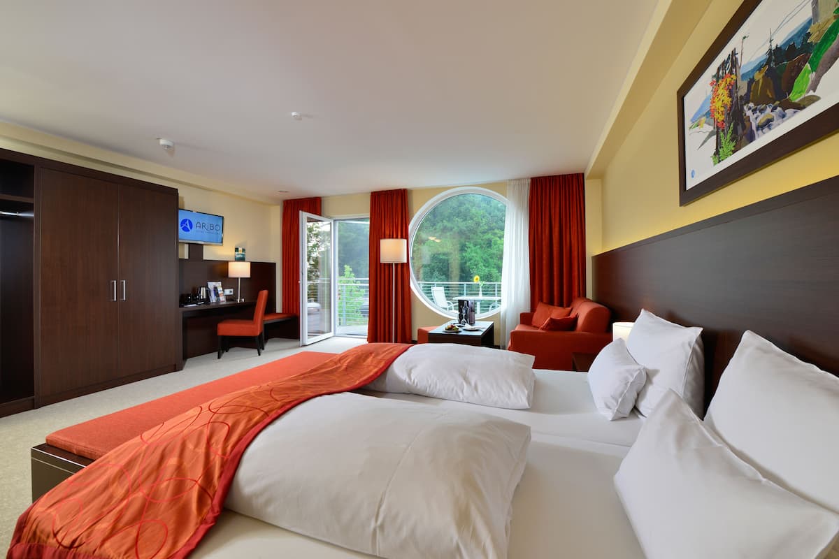 Une chambre d’hôtel avec un grand lit, un bureau avec un ordinateur, une chaise et une vue sur la verdure.