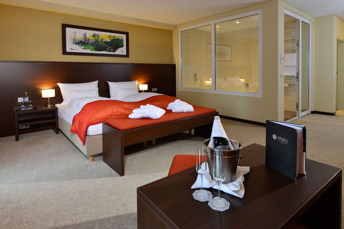 Une chambre d’hôtel avec un lit, une table de chevet, un bureau avec une bouteille de champagne et un verre.