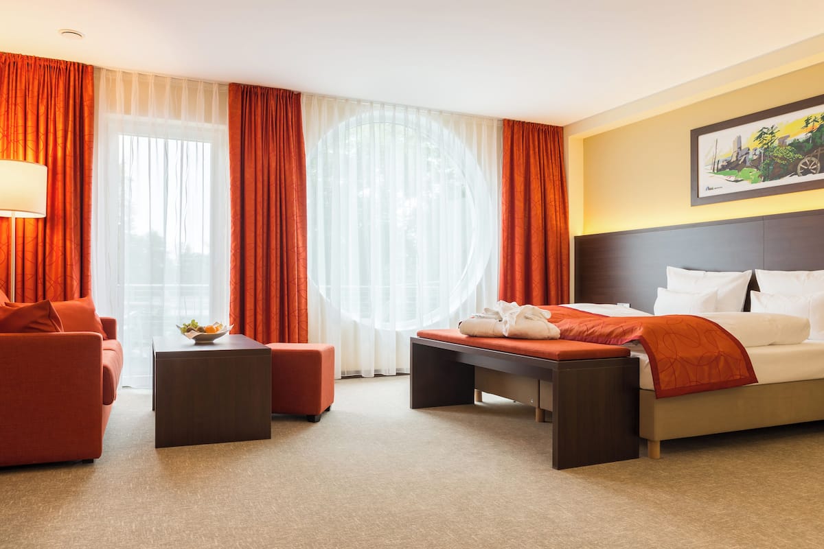 Une chambre d’hôtel avec un lit, un canapé, une petite table et une grande fenêtre avec des rideaux.