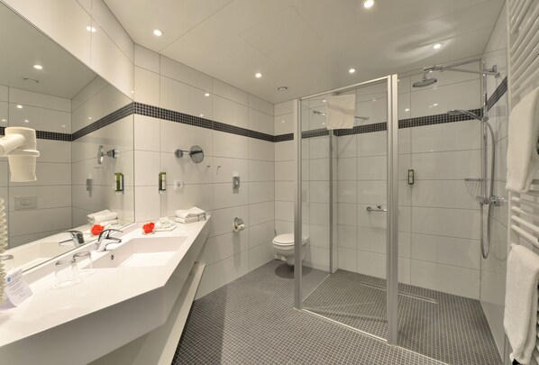 A modern bathroom with a glass-enclosed shower, a white sink with a mirror, and a toilet.