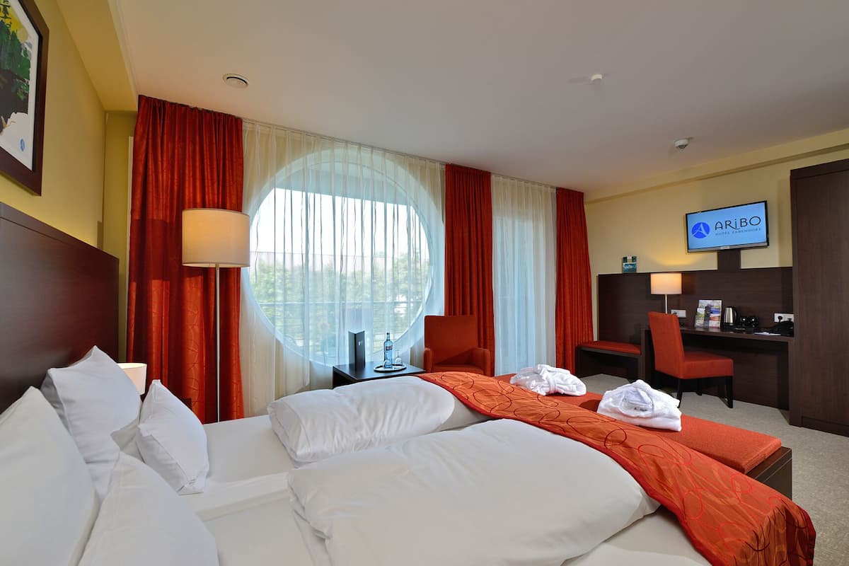 Une chambre d’hôtel avec deux lits, un bureau, une télévision et une grande fenêtre avec des rideaux.