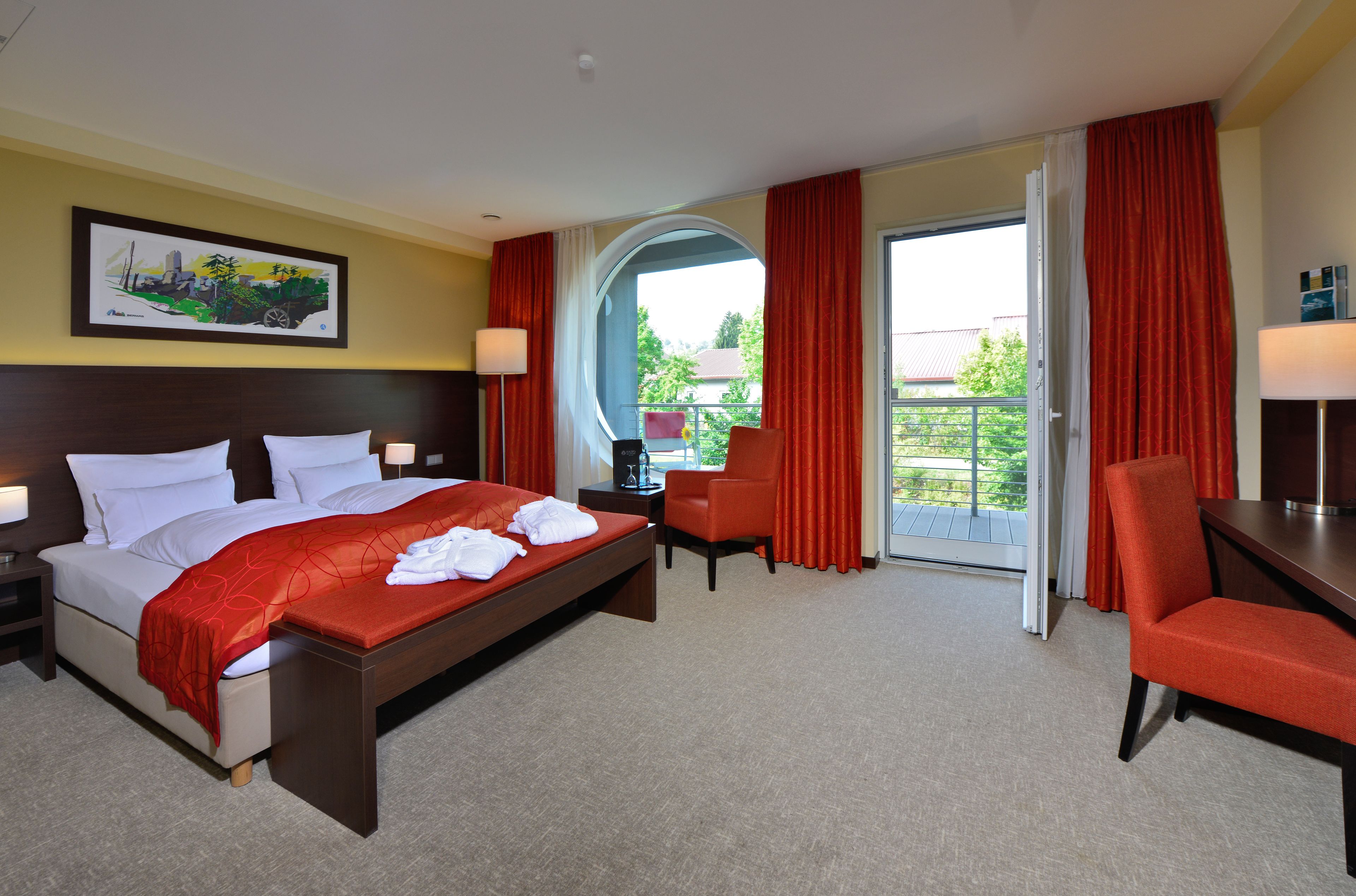Ein Hotelzimmer mit einem Bett, zwei Stühlen, einem Schreibtisch, einer Lampe und einem Bild an der Wand.