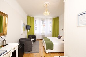 A hotel room with a bed, a desk, a chair, a television, and a chandelier. - Hotel Emma (Östersund)
