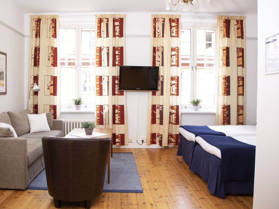 A room with a sofa, a chair, a bed, a TV, and curtains with a geometric pattern.