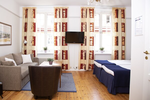 A room with a sofa, a chair, a bed, a TV, and curtains with a geometric pattern. - Hotel Emma (Östersund)