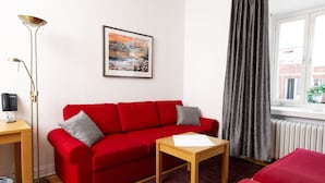 Un sofá rojo, una mesita de madera, una lámpara de pie y una ventana con cortinas.