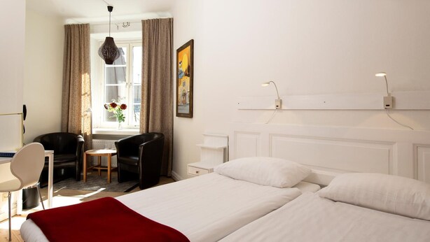 Una habitación de hotel con cama, escritorio, silla y ventana con cortinas.