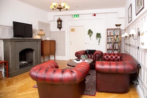 A living room with a fireplace, leather sofas, a television, and a bookshelf. - Hotel Emma (Östersund)