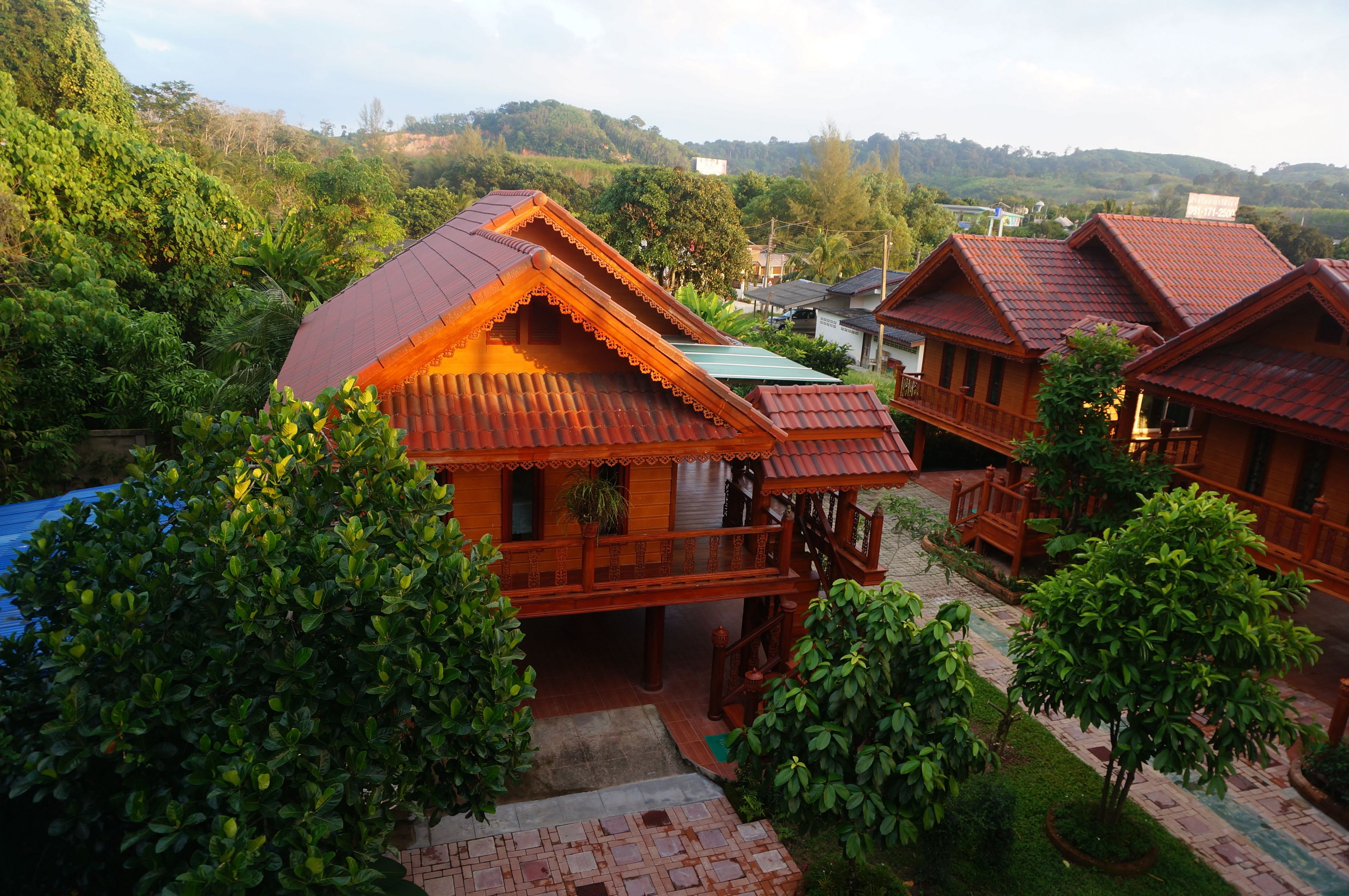 Una casa de madera tradicional con techo inclinado, rodeada de abundante vegetación y un paisaje montañoso al fondo.