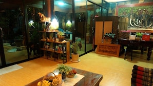 A cozy living room with a wooden coffee table, a sofa, and a glass partition. There are potted plants and decorative items on shelves. - Ruenthai Boutique (Sa Khu)