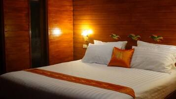 A hotel room with a wooden paneled wall, a bed with white linens and an orange accent pillow, and a wall-mounted light fixture.