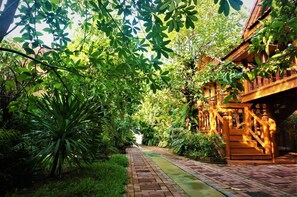 A pathway leading to a traditional wooden building surrounded by lush greenery. - Ruenthai Boutique (Sa Khu)