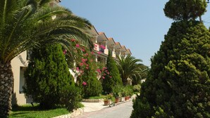 A row of buildings with balconies, surrounded by lush greenery and palm trees. - Letsos Hotel (Zakynthos)