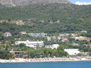 Une zone côtière avec des bâtiments construits sur une colline, une plage parsemée de parasols et une vue dégagée sur la mer.