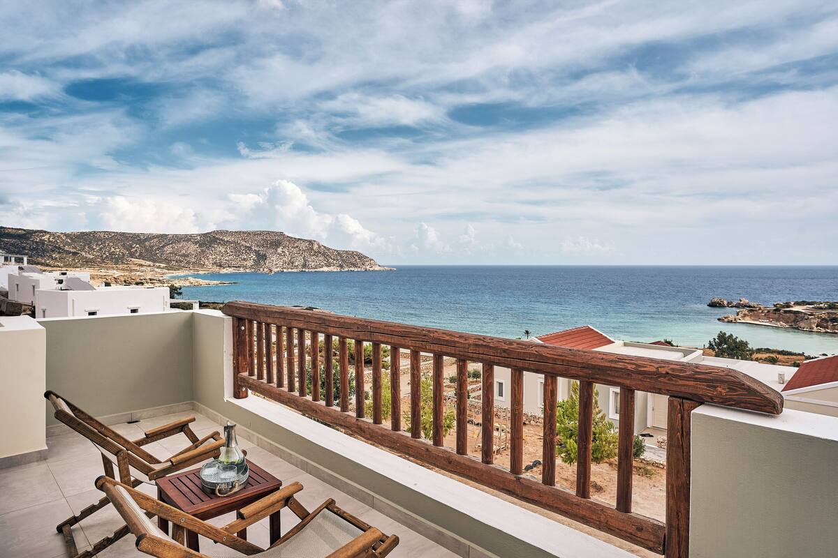 A balcony with wooden railings overlooking a coastal view, featuring a table and chairs.