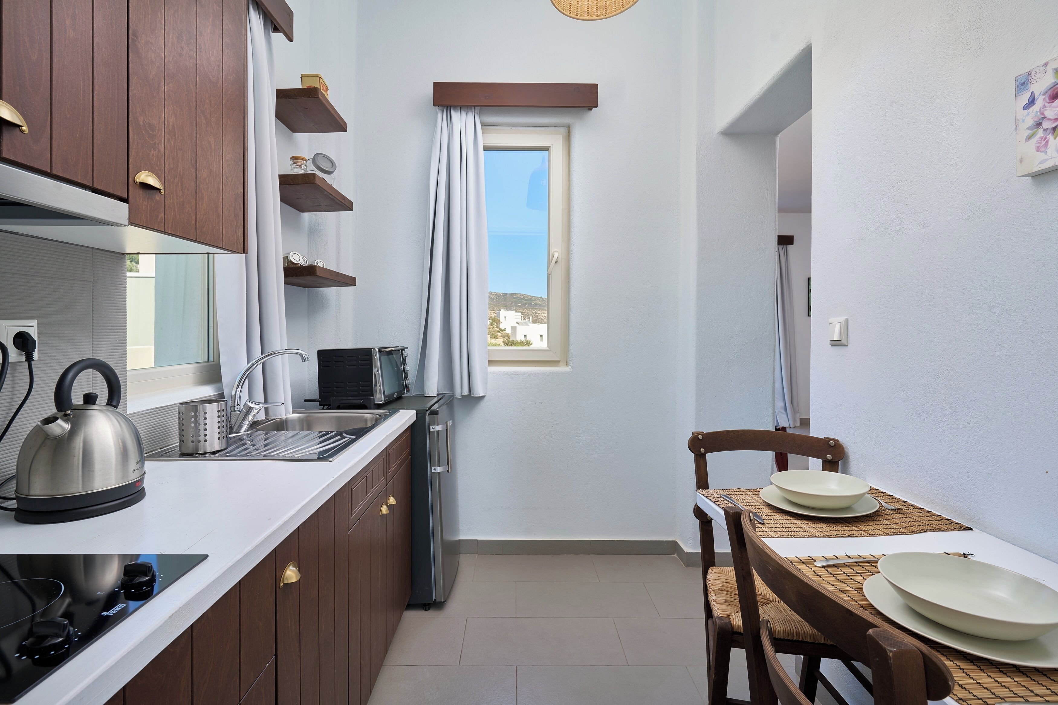 A compact kitchen with wooden cabinets, a kettle, a toaster, and a small refrigerator.