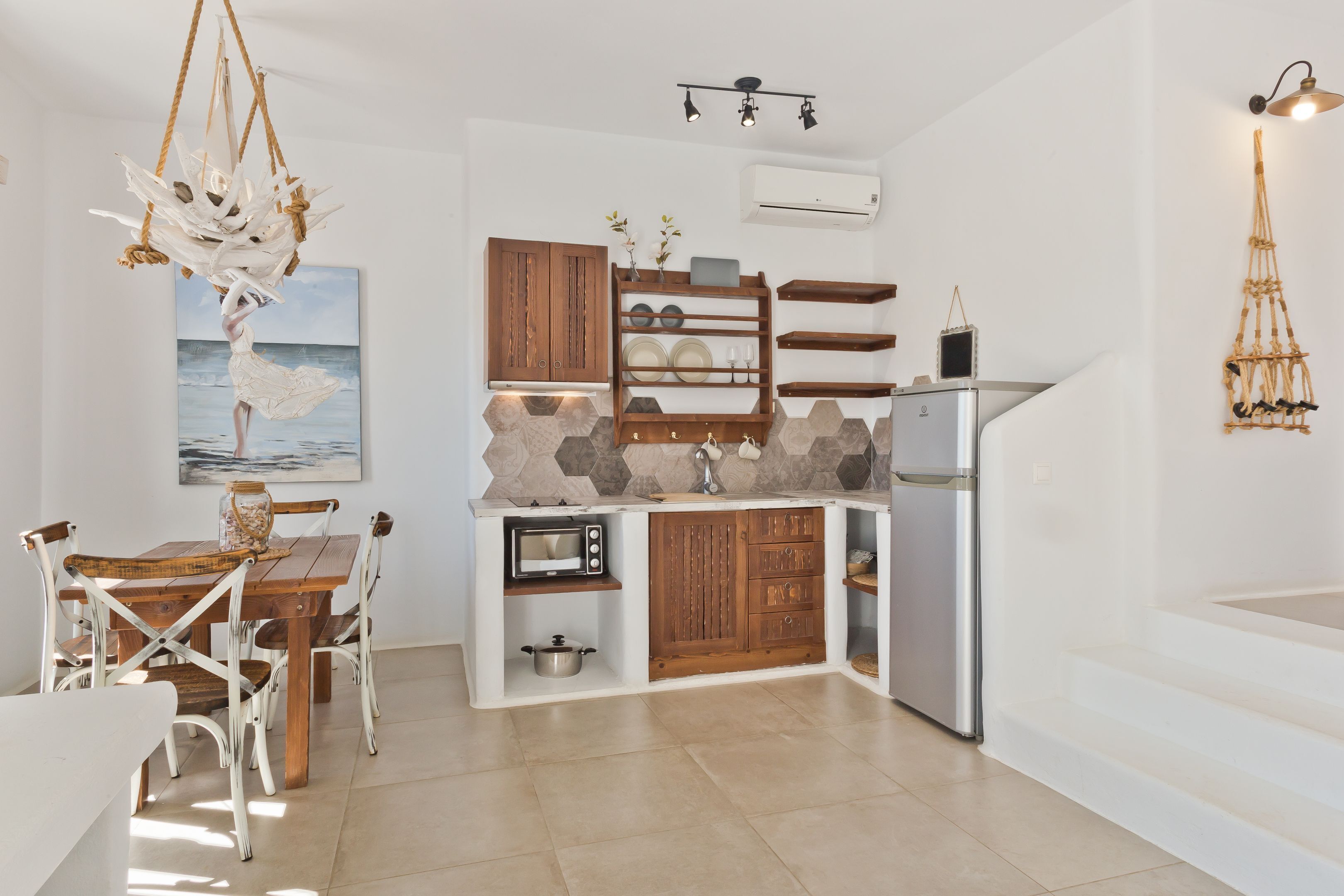 Cocina compacta con una mesa de comedor de madera, sillas blancas, microondas integrado y refrigerador.