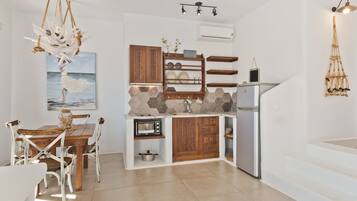 Cocina compacta con una mesa de comedor de madera, sillas blancas, microondas integrado y refrigerador.