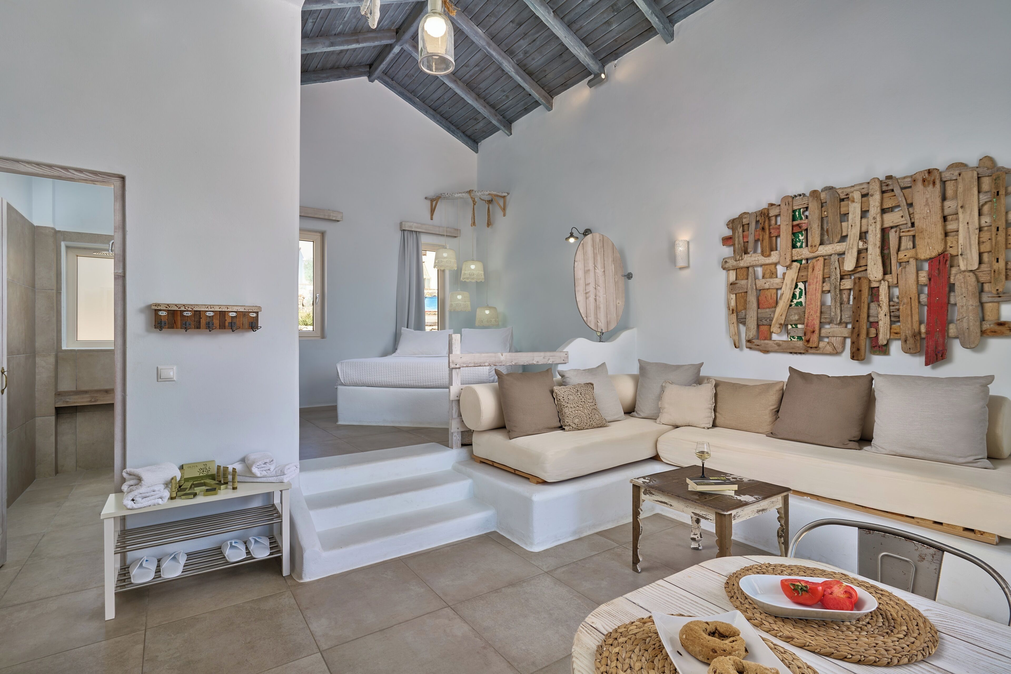 A spacious living area with a white sofa, a wooden wall art piece, and a dining table with a placemat.