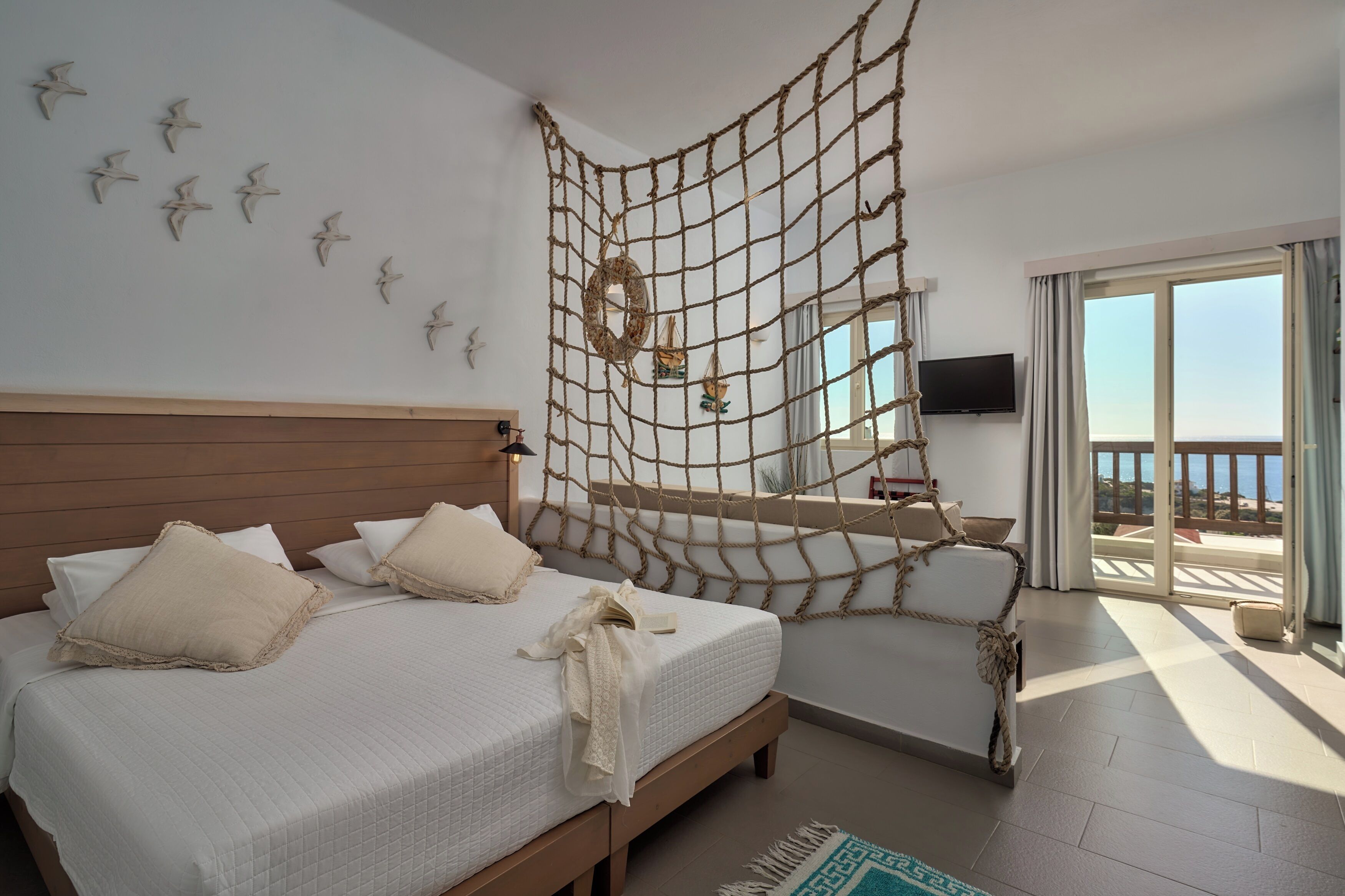 A bedroom with a bed, a netted wall decoration, a television, and a balcony with a view.
