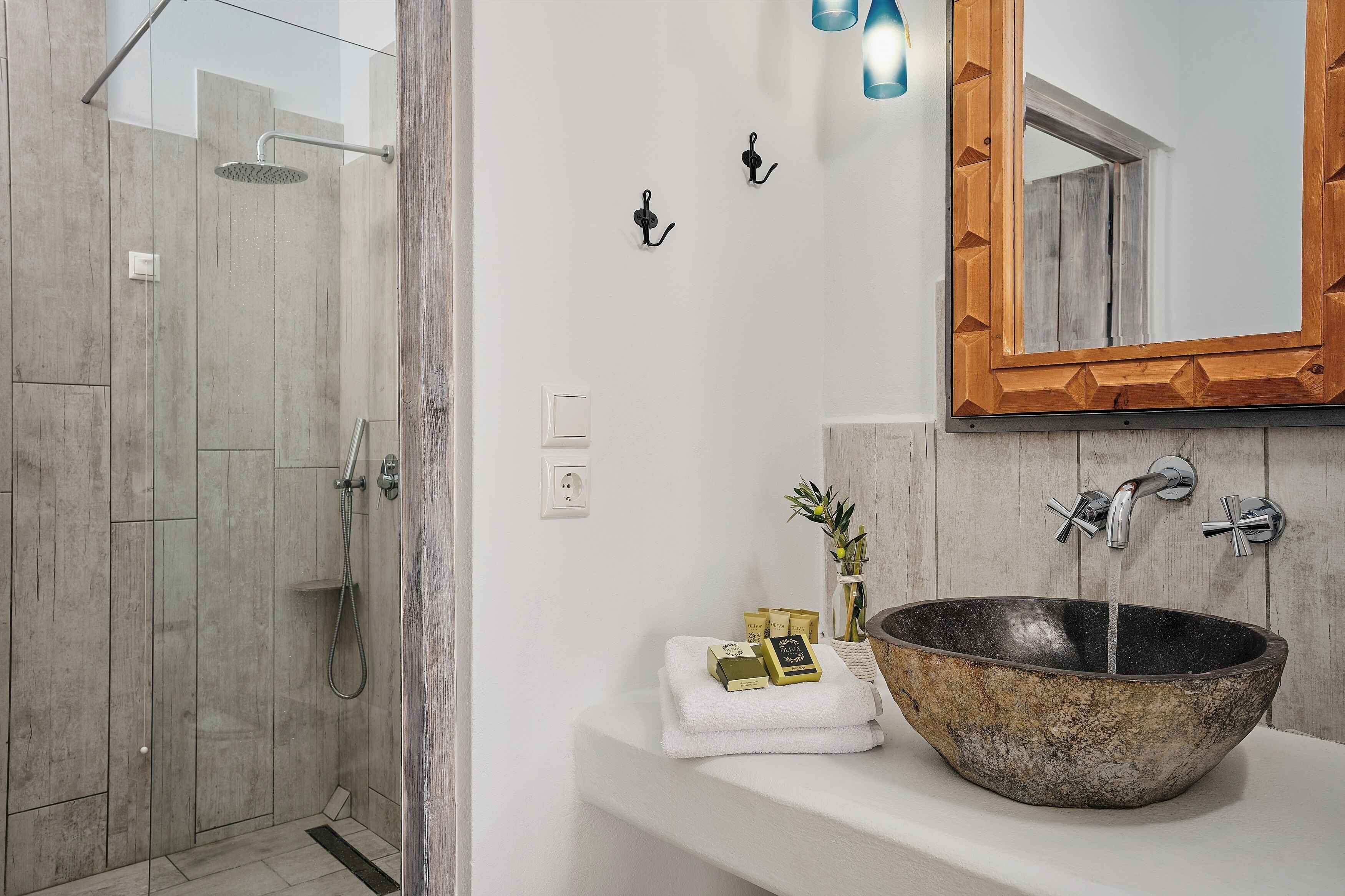 A modern bathroom with a glass-enclosed shower, a large vessel sink, and a wooden-framed mirror.