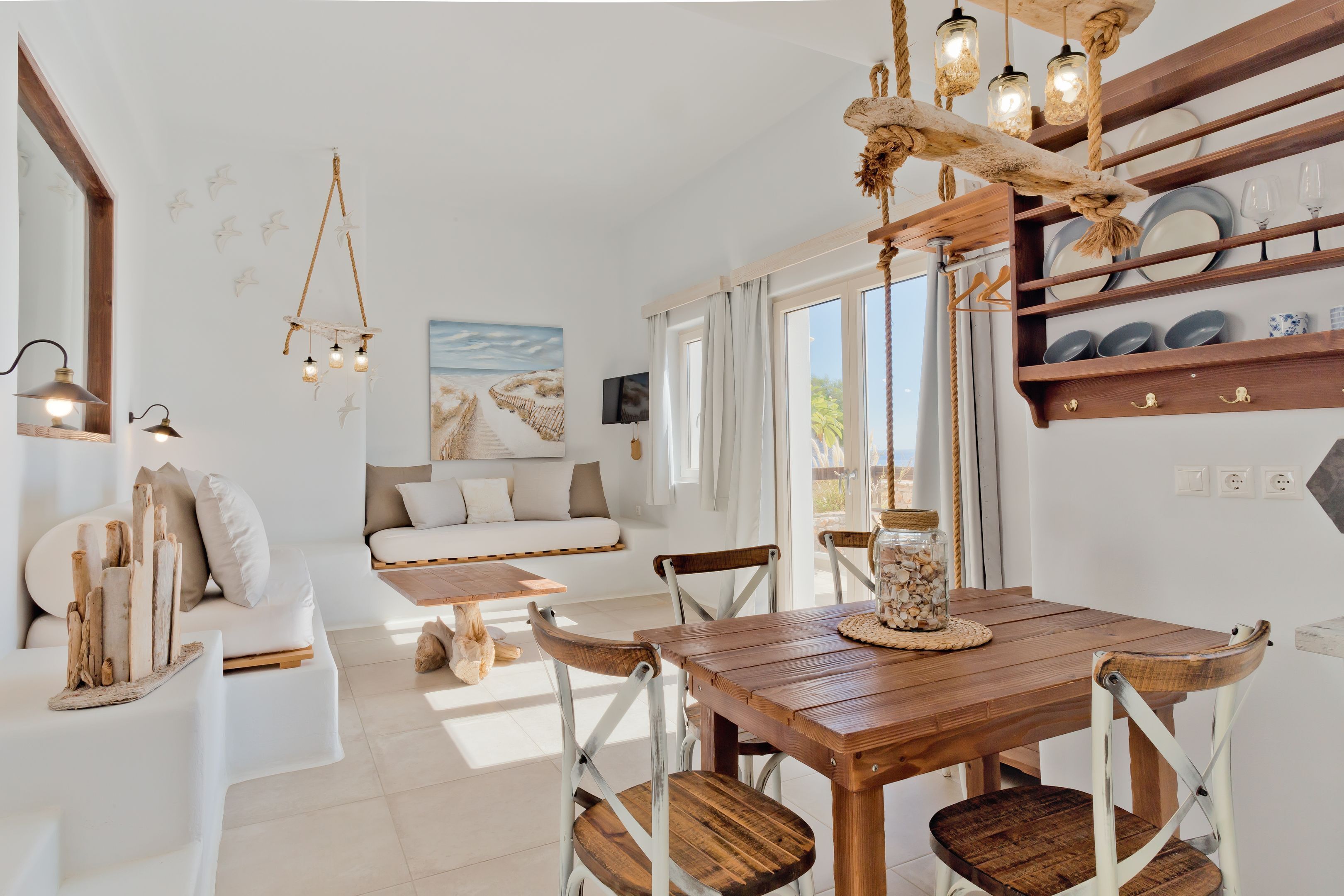A modern living room with a wooden dining table, white sofa, and a large window with curtains.