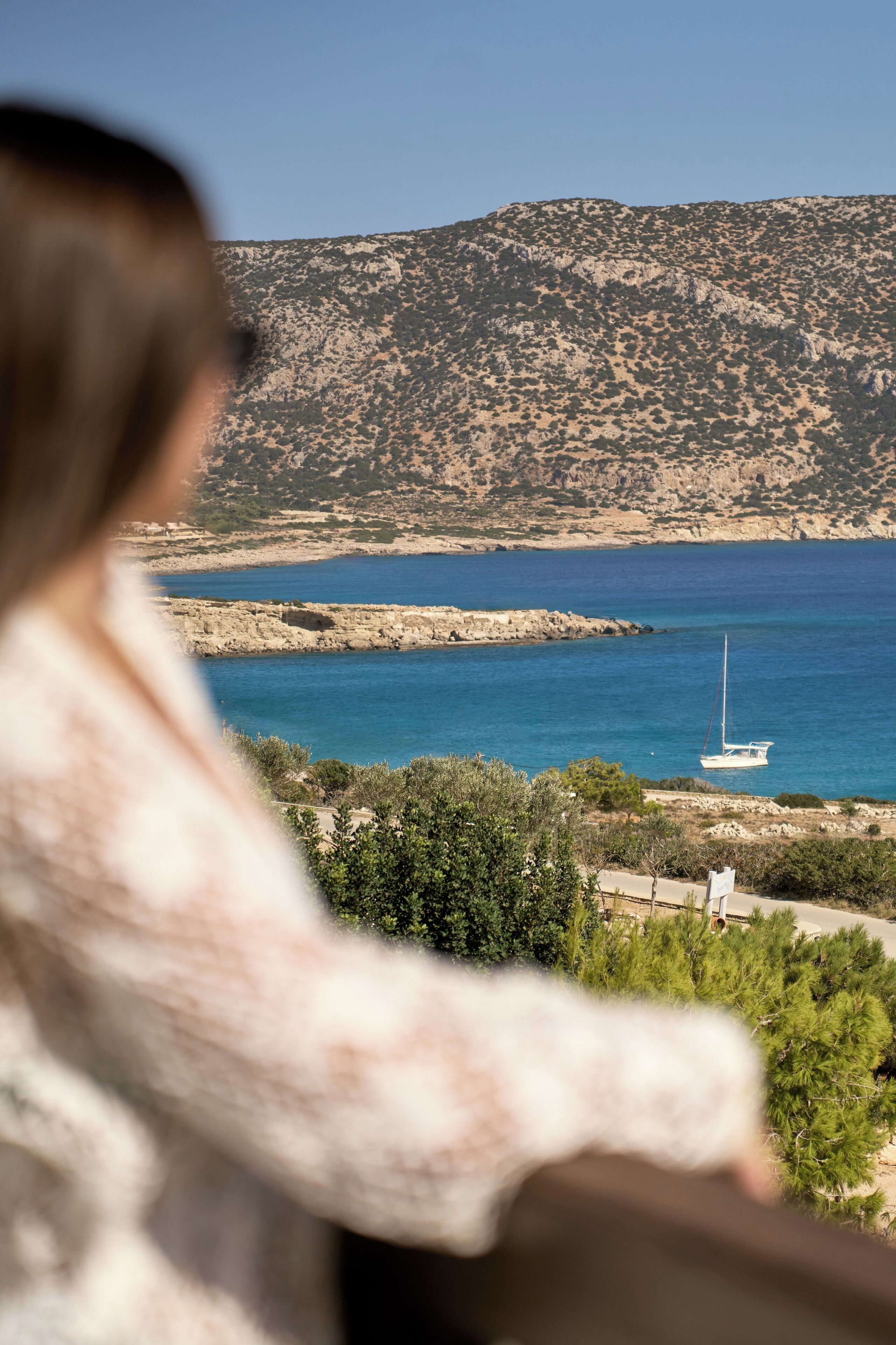A coastal landscape with a rocky shoreline, a sailboat, and a person overlooking the scene.