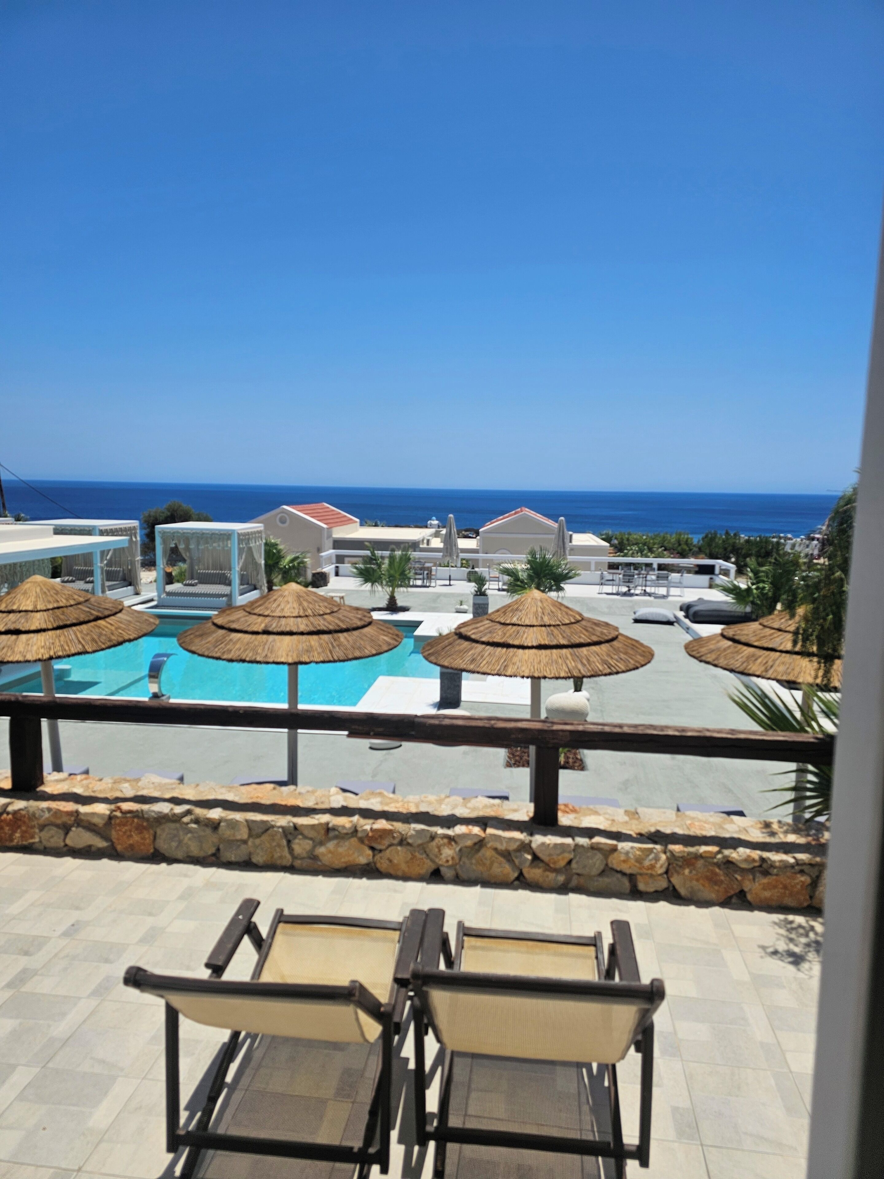 Ein Poolbereich mit Sonnenschirmen, Liegestühlen und Blick aufs Meer.