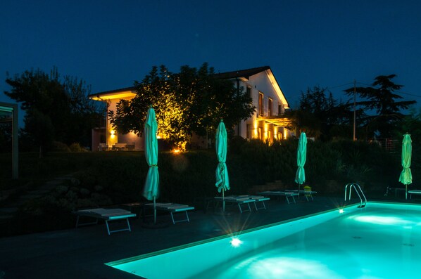 A swimming pool with lounge chairs and umbrellas, a house in the background, and a well-lit exterior. - Casa LuceSole (Fontanile)
