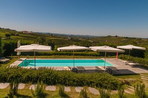 A swimming pool with lounge chairs and umbrellas, surrounded by greenery and vineyards. - Casa LuceSole (Fontanile)
