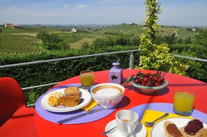 A table with breakfast items including coffee, juice, and a bowl of cherries, set against a scenic vineyard backdrop. - Casa LuceSole (Fontanile)