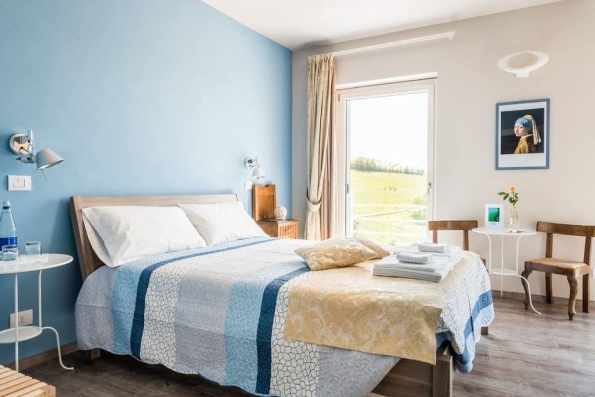 A bedroom with a bed, bedside tables, a window with curtains, and a view of the outdoors.