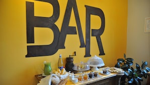 Un espace bar avec une grande enseigne « BAR », une table de buffet proposant divers plats, un appareil à café et une carafe contenant une boisson verte.