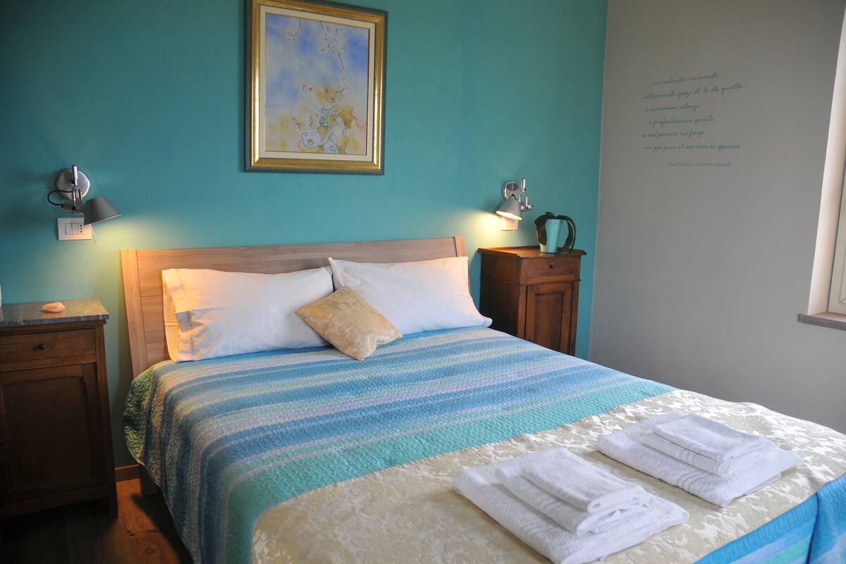 A neatly made bed with a striped bedspread and two pillows, a bedside table with a lamp, and a framed artwork on the wall.
