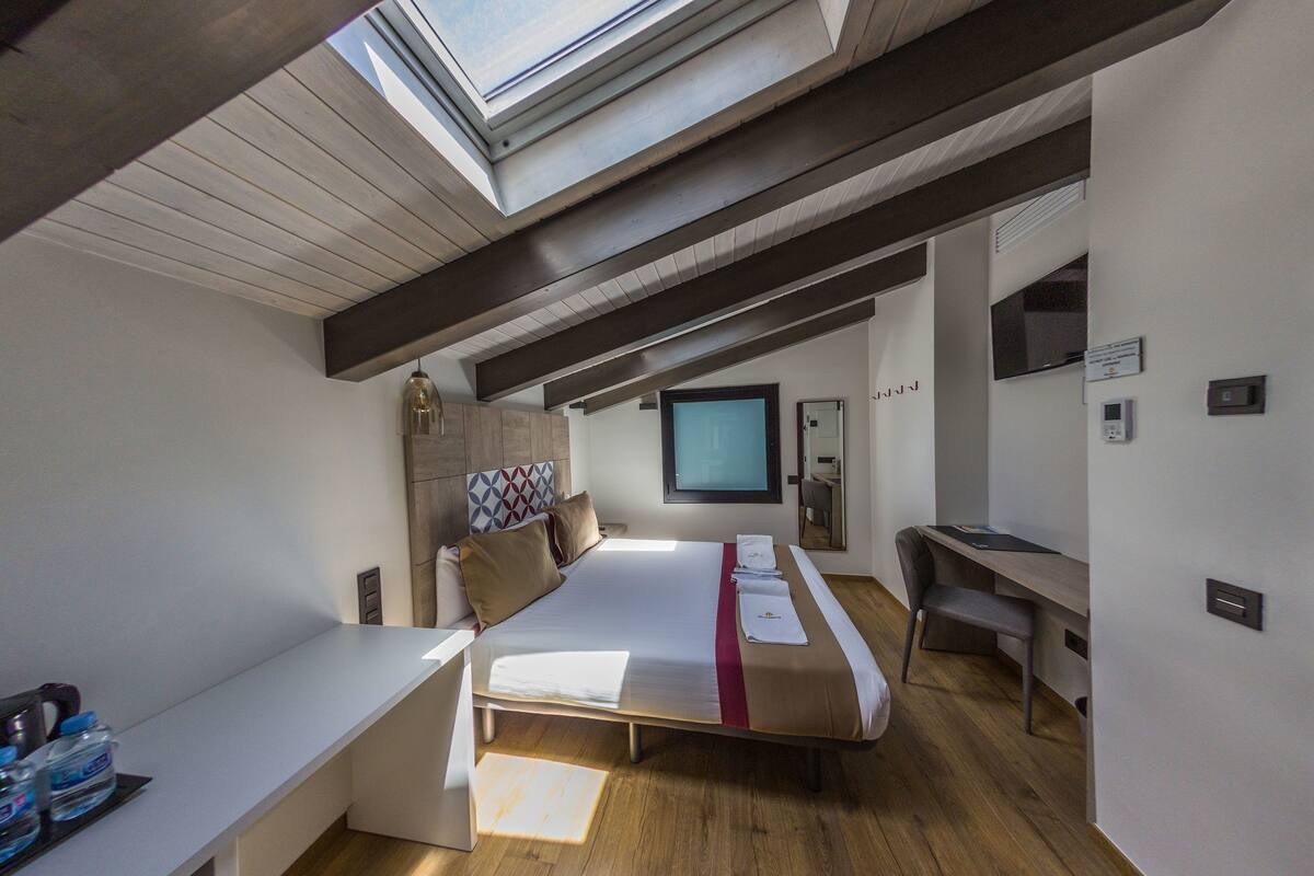 A modern hotel room with a skylight, a bed, a desk, and a TV.