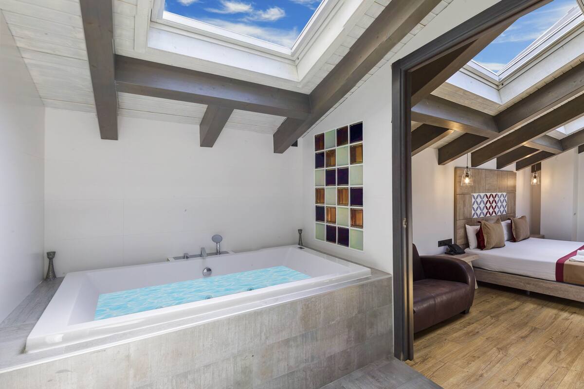 A modern room with a skylight, a large bathtub, a bed, and a wooden floor.