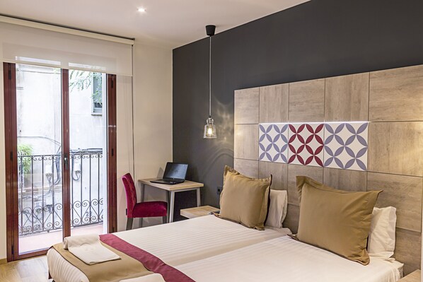 A hotel room with a bed, a desk with a laptop, a chair, and a view of the outside balcony. - Boutique Hostemplo Sagrada Familia (Barcelona)