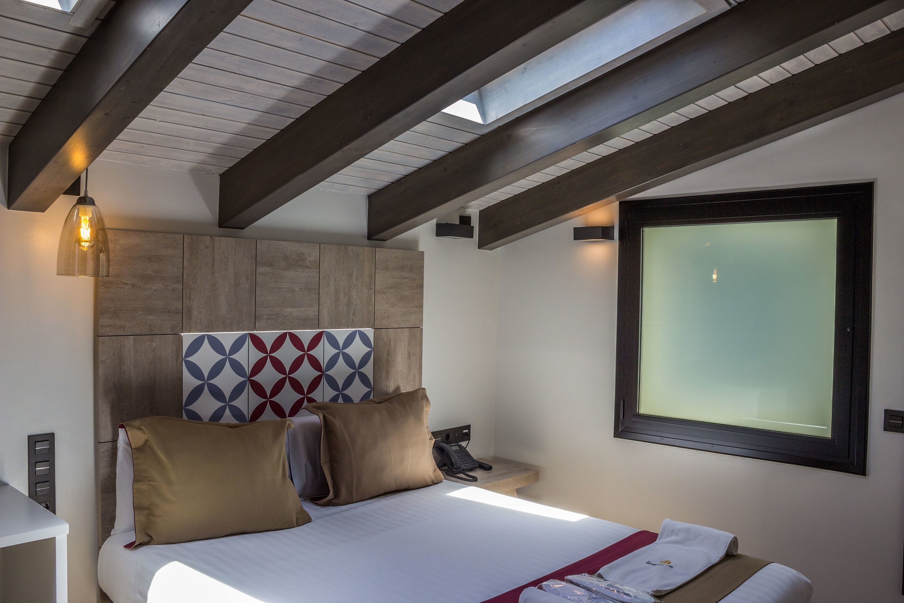 Une chambre d’hôtel comprenant un lit, une table de chevet, un téléphone et une fenêtre avec du verre dépoli.