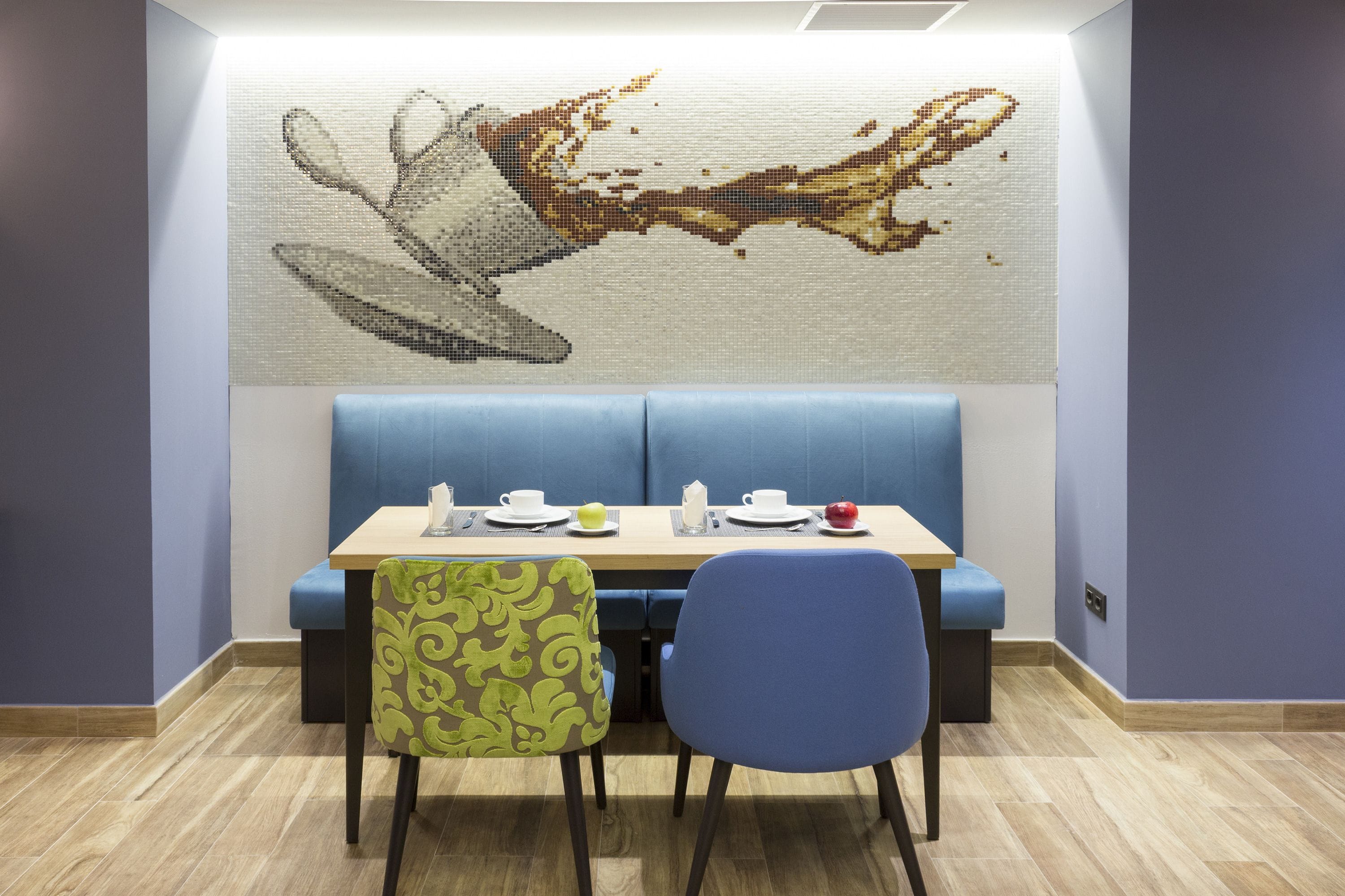 A dining area with a table set for two, a blue cushioned bench, and a wall-mounted artwork.