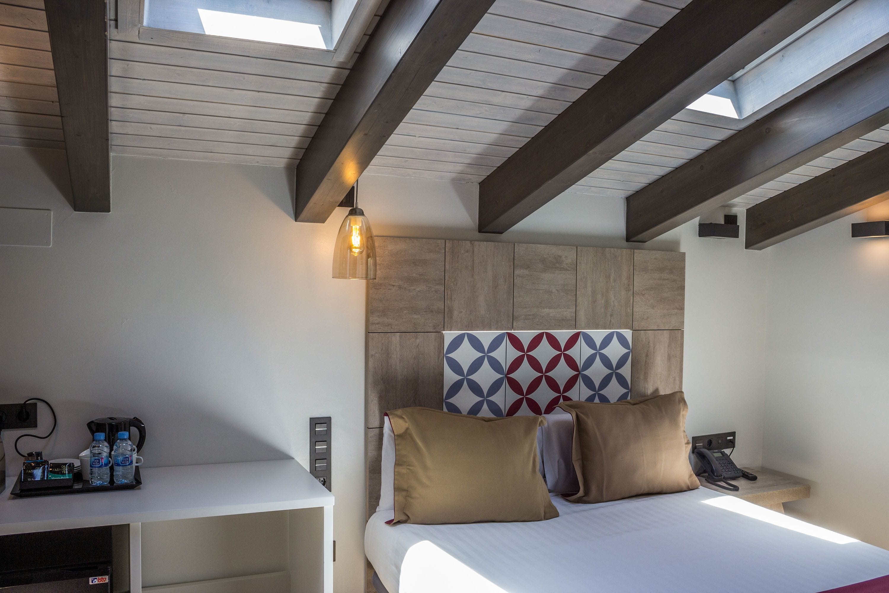 Ein Hotelzimmer mit einem Bett, einem Schreibtisch mit Telefon und Lampe sowie einer Wand mit geometrischem Muster.