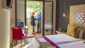 A hotel room with a bed, a desk with a laptop, a red chair, and a view of the outside. - Boutique Hostemplo Sagrada Familia (Barcelona)