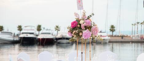 A table set for a wedding reception with white chairs and a floral centerpiece.