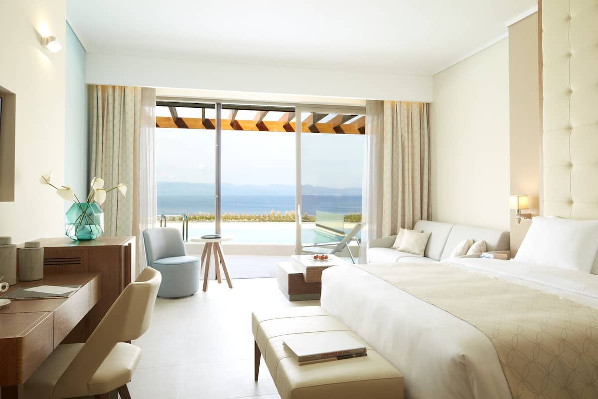Ein Hotelzimmer mit einem großen Bett, einem Schreibtisch, einem Sessel und Blick auf den Ozean.