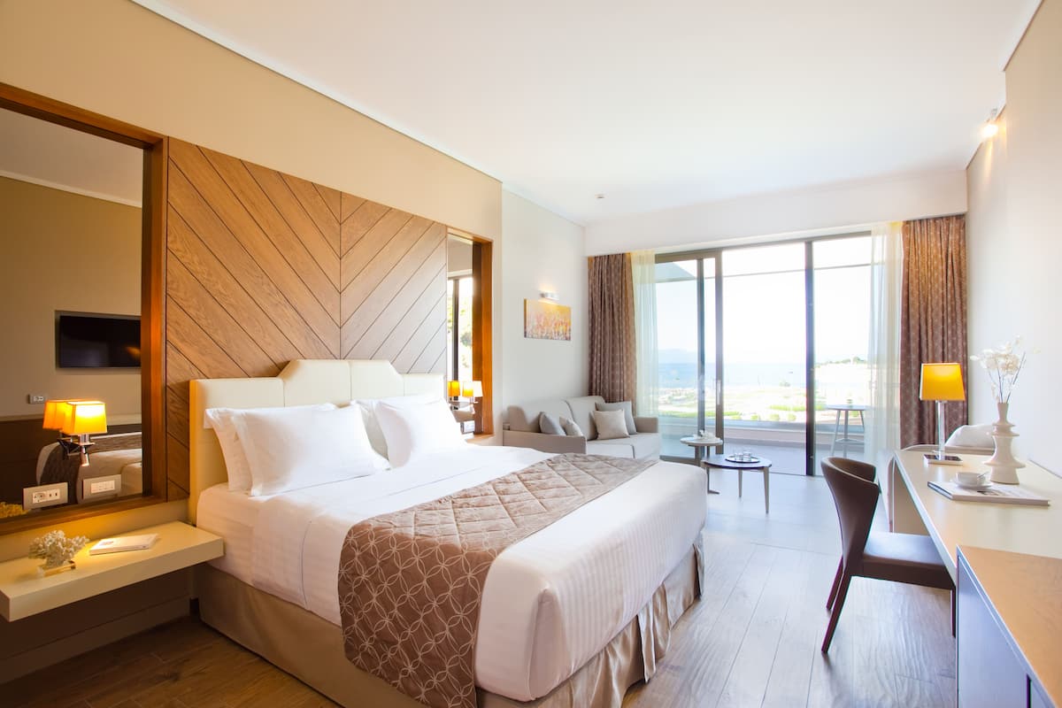 Ein Hotelzimmer mit einem großen Bett, einem Schreibtisch, einem Sessel und einer Couch, mit Blick ins Freie.
