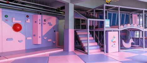 Un espace de jeux doté d’un sol rembourré, d’un mur d’escalade et d’une structure de jeux en forme de filet.