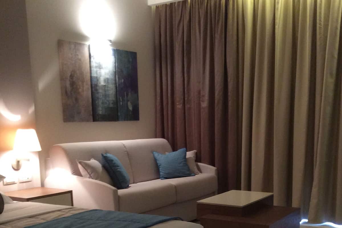 Ein Hotelzimmer mit Bett, Sofa, Couchtisch, Lampe und einem Bild an der Wand.